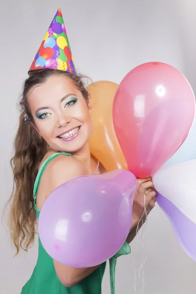 Bruna donna in un cappello di compleanno che tiene palloncini e sorride felicemente — Foto Stock