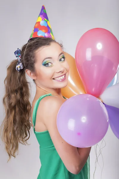 Brunette vrouw in een verjaardag cap bedrijf ballonnen en gelukkig glimlach — Stockfoto