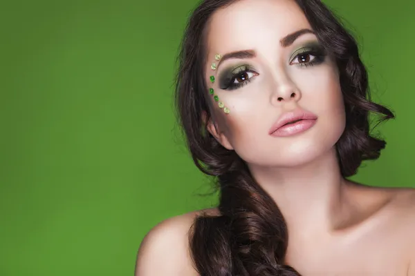 Beautiful brunette dryad woman with creative make up and beads on her face, curly hair and costume made of leaves on green background. Copy Space — Stock Photo, Image