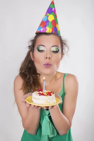 Bruna donna in un cappello di compleanno che soffia la candela sulla torta — Foto Stock