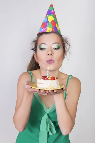 Brünette Frau mit Geburtstagskappe bläst die Kerze auf Kuchen — Stockfoto