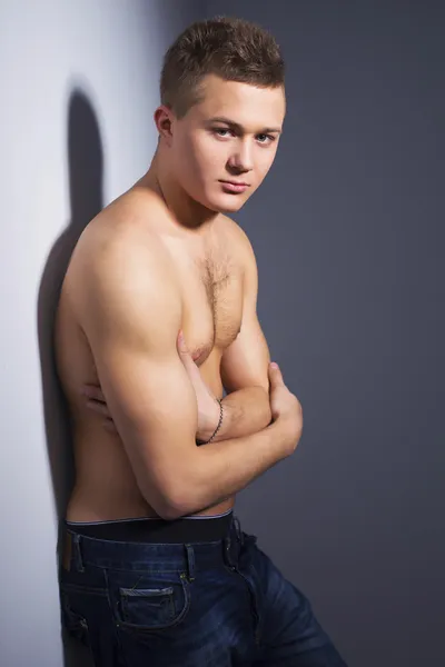 Shirtless handsome man with fit body lean against a wall indoor