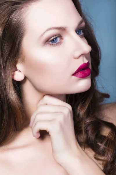 Bella donna bruna con trucco creativo ombretti viola labbra rosse piene, occhi blu e capelli ricci con la mano sul viso — Foto Stock