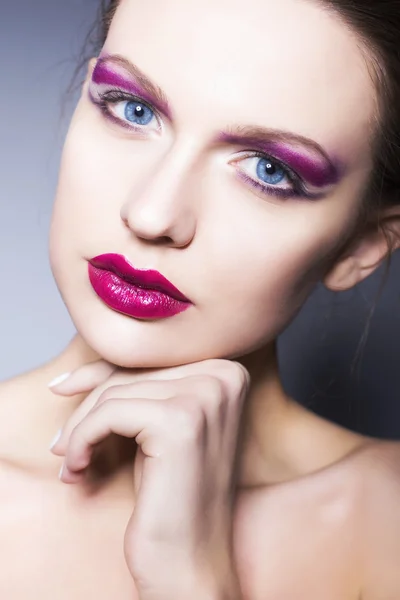 Beautiful brunette woman with creative make up violet eye shadows full red lips, blue eyes and curly hair with her hand on her face — Stock Photo, Image