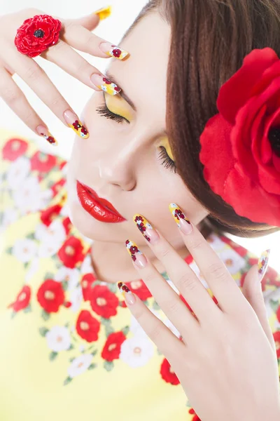 Donna bruna in abito giallo e rosso con fiore di papavero nei capelli, anello di papavero e unghie creative, occhi chiusi su sfondo bianco — Foto Stock