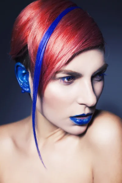 Young person with blue eye shadows, blue ears and pink hair with blue strand on it looking at camera and hands near face. Black background — Stock Photo, Image