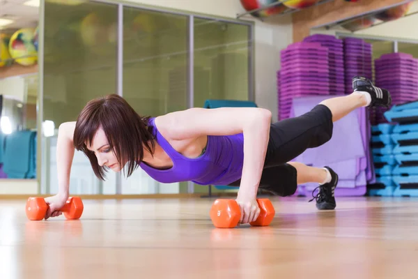 Donna in forma facendo flessioni con manubri su un pavimento in una palestra sorridente — Foto Stock