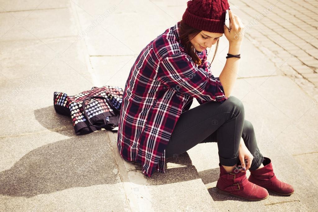Brunette woman in hipster outfit sitting on steps on the street. Toned image. Copy Space