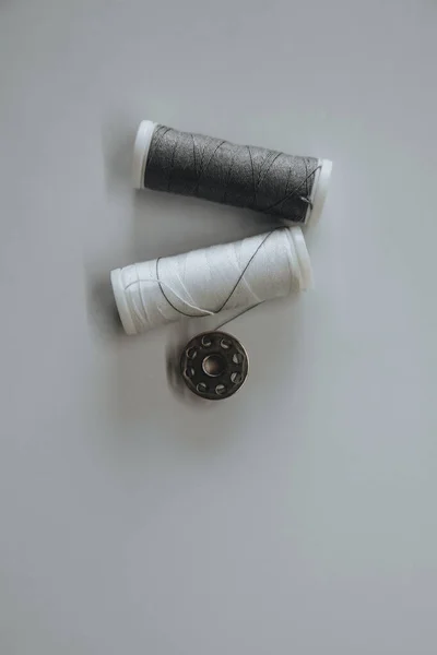 Two spools of white and gray thread and a button lie on a light background — Stock Photo, Image