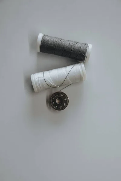 Two spools of white and gray thread and a button lie on a light background Fotografia De Stock