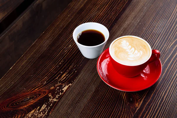 우유와 라떼 아트와 테이블 위에 하얀 컵에 커피를 탄 빨간 컵에 담긴 커피 — 스톡 사진