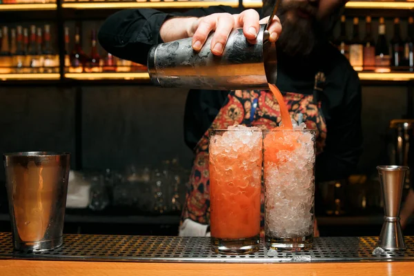 Profesyonel bir barmen iki kırmızı kokteyl yapar, karıştırıcıdan bir kokteyl döker. Kokteyller barda..