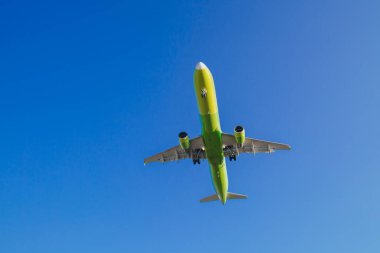 Sarı-yeşil renkli yolcu uçağı mavi gökyüzünde beyaz bulutlar, hava taşımacılığı konsepti, nüfus tahliyesi ile uçar..