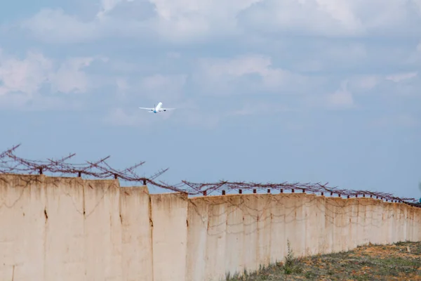 Gökyüzündeki uçak, dikenli tellerle çevrili beton bir duvarın arka planında. Tahliye. Suç, kaçış — Stok fotoğraf