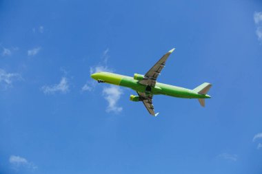 Sarı-yeşil renkli yolcu uçağı mavi gökyüzünde beyaz bulutlar, hava taşımacılığı konsepti, nüfus tahliyesi ile uçar..