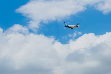 Gökyüzünde uçan beyaz-mavi yolcu uçağı arka planda inanılmaz bulutlar, hava taşımacılığı, nüfus tahliyesi.
