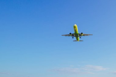 Passenger plane of yellow-green color flies in the blue sky, air transportation concept, population evacuation.
