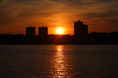 Turuncu ve yuvarlak güneş gökdelenlerin arkasına gidiyor ve New York 'taki Hudson Nehri' ni aydınlatıyor.