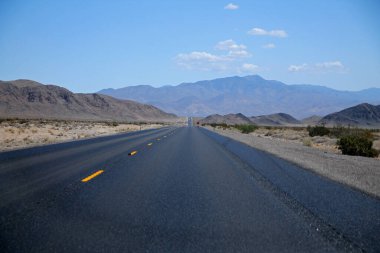 Kaliforniya Çölü 'nde uzun bir asfalt sokağın sonundaki dağlar berrak mavi bir gökyüzünün altında.