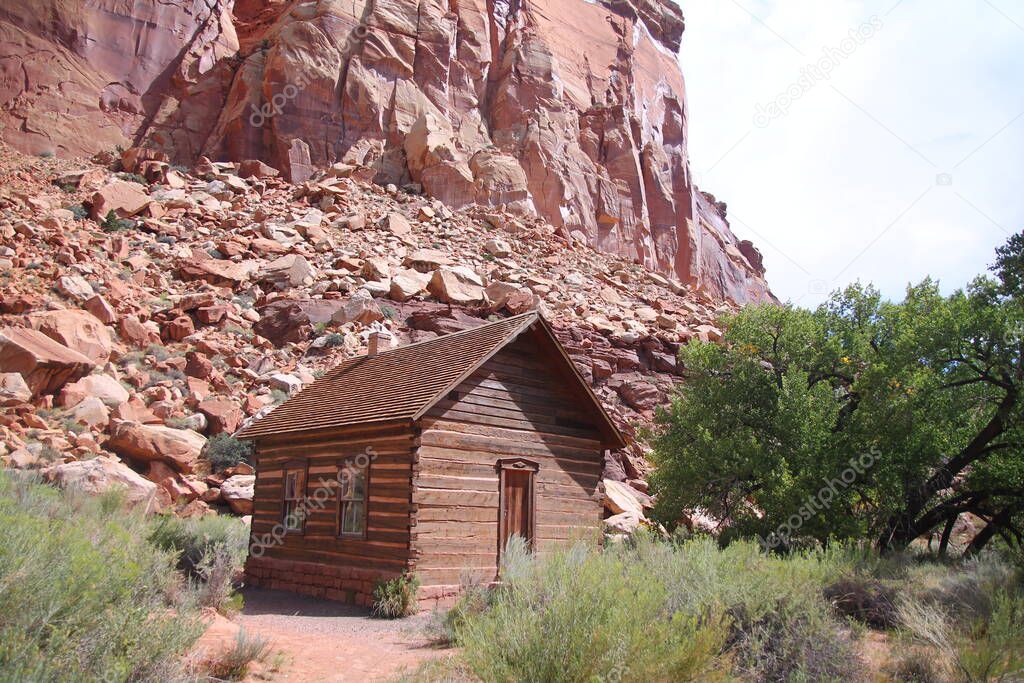 The tiny small Fruita Schoolhouse with the red rock cliff on the back in Utah