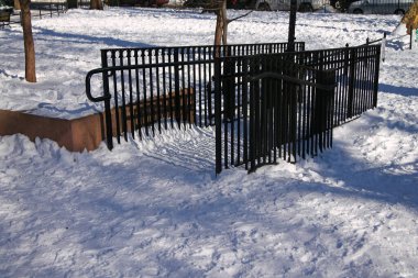 Güneşli bir kış gününde parktaki beyaz kar üzerinde siyah bir çit.