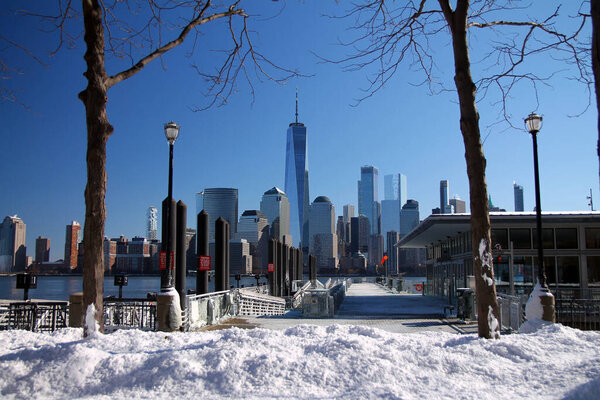 Downtown Manhattan and the Freedom tower with a ferry dock and the snow from the other side of the Hudson River in Jersey City