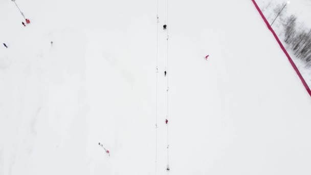 Vista superior panorámica desde el dron por cable en la estación de esquí. Ascensor de esquí que transporta esquiadores y snowboarders en la pista de invierno nevada en la estación de montaña, muchas personas. UHD 4k video — Vídeo de stock