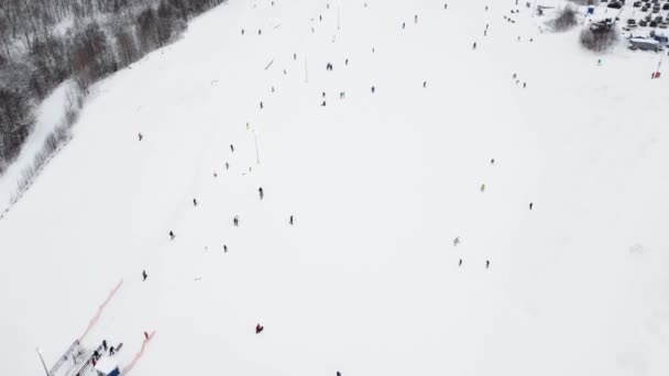 スキー場のケーブルウェイでドローンからのパノラマのトップビュー。マウンテンリゾートの雪の冬の斜面にスキーヤーやスノーボーダーを運ぶスキーリフトエレベーター、多くの人々。UHD 4kビデオ — ストック動画