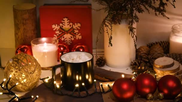 Décorations de Noël, lumières clignotantes, Nouvel An 2022, fond 4k. Cadeau de Noël, tasse de café, boules rouges, bougie, cônes de sapin, bouteilles. — Video