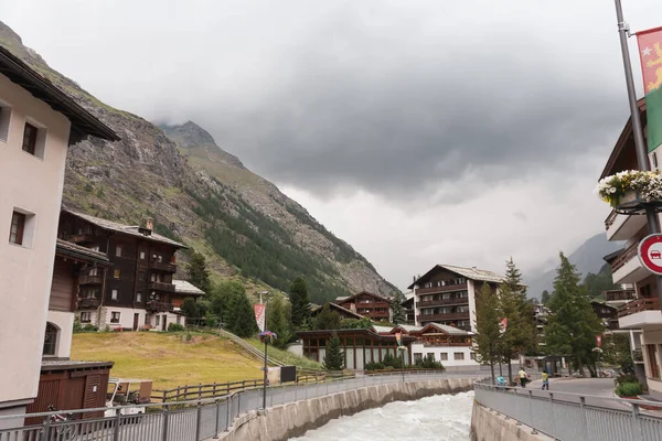Bergsflod i en by i schweiziska Alperna. Traditionella alpina trähus. Himmel före åskväder. — Stockfoto