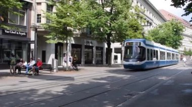 İsviçre, Zürih, Temmuz 2019: Seçkin dükkanları olan ünlü Central City Caddesi. Güneşli bir günde caddede hareket eden tramvaylar bulutların stok görüntüleriyle, 4K