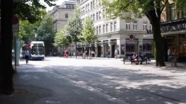 İsviçre, Zürih, Temmuz 2019: Seçkin dükkanları olan ünlü Central City Caddesi. Güneşli bir günde caddede hareket eden tramvaylar bulutların stok görüntüleriyle, 4K