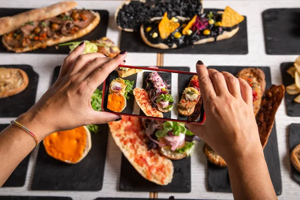 A female food blogger takes photos of the dishes on the restaurant table. Top view. Friends lunch, social media backgrounds