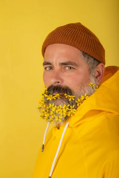 Sakalında çiçekler olan çekici sakallı bir adam, sarı arka planda soyutlanmış. Dikey görünüm