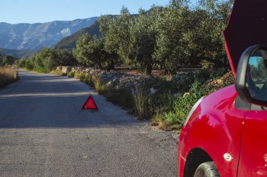 İkincil yolun hendeğinde açık kapüşonlu ve uyarı üçgenli hasarlı bir araba..