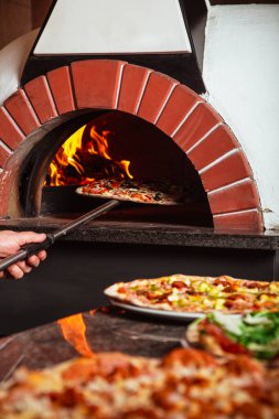 Şef pizzayı alır. İtalyan pizzası odun ateşinde pişirilir.