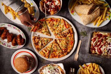 Bir misafirin eli, restoran masasında bir dilim pizza alır.