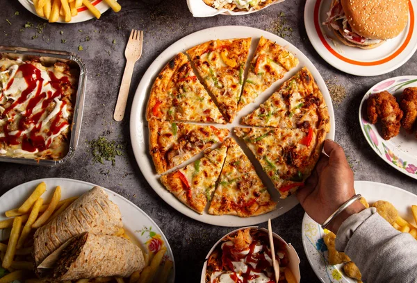 Bir adamın eli fast food restoranındaki masadan bir dilim pizza alıyor.