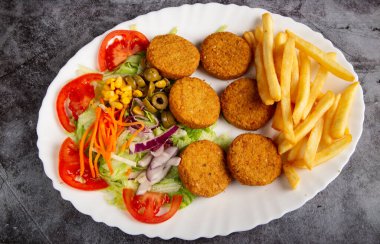 Oval dish of traditional falafel potatoes along with fries and salad.