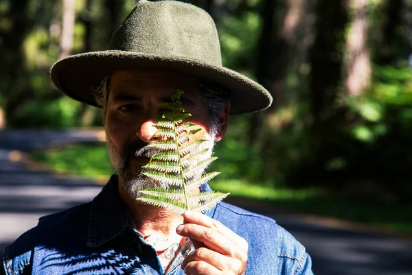 Earth day and love for nature concept with attractive man with a fern leaf covering one eye and enjoying nature leisure activity outdoors.