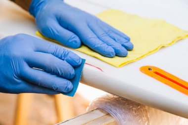 Surfer with protective gloves sanding a repair on the surfboard.