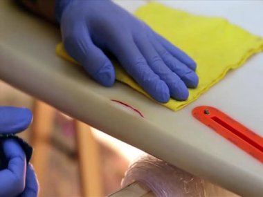 Surfer with protective gloves sanding a surfboard. home repair