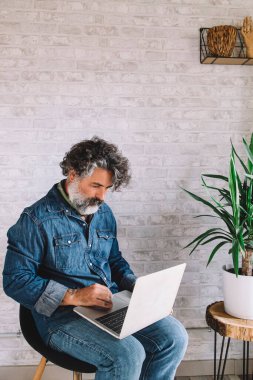 Serious man working on laptop online, sitting on chair, looking at computer screen, focused man using internet banking service, typing email, looking for information
