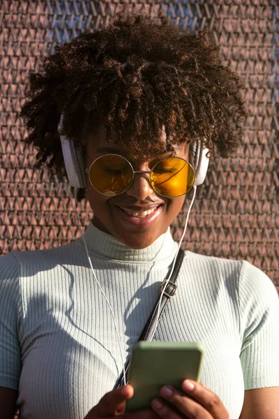 Cool young latin american woman with afro hair and glasses smiling using smartphone for social networks.