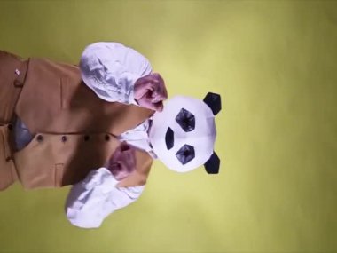 Aptal adam sarı bir arka planda pandanın maskesiyle dans edip kutlama yapıyor. Dikey biçimdeki video