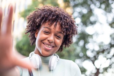Avrupa 'da güzel bir günde enerjisini ifade eden genç bir melez kadın modelin portresi. Kulaklıklı çekici bir afro kadın şehirde dolaşırken selfie çekiyor..