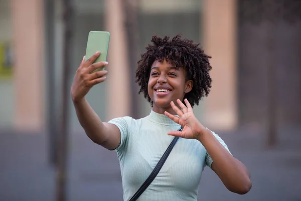 Happy female blogger with afro hair laughing, holding phone, recording vlog, shooting social media story or video call on mobile app.
