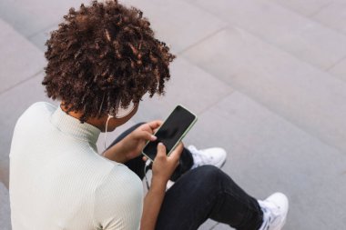 Akıllı telefonuyla mesaj yazan kıvırcık saçlı genç bir kadın, cep telefonunu kullanarak kıvırcık saçlı bir Latin.
