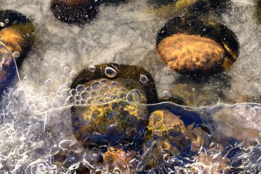 Kayalar donmuş bir göldeki yarı erimiş buzu delip geçer.