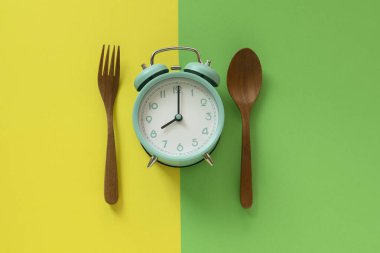 Food clock spoon and fork, Healthy food breakfast concept on yellow and green table background